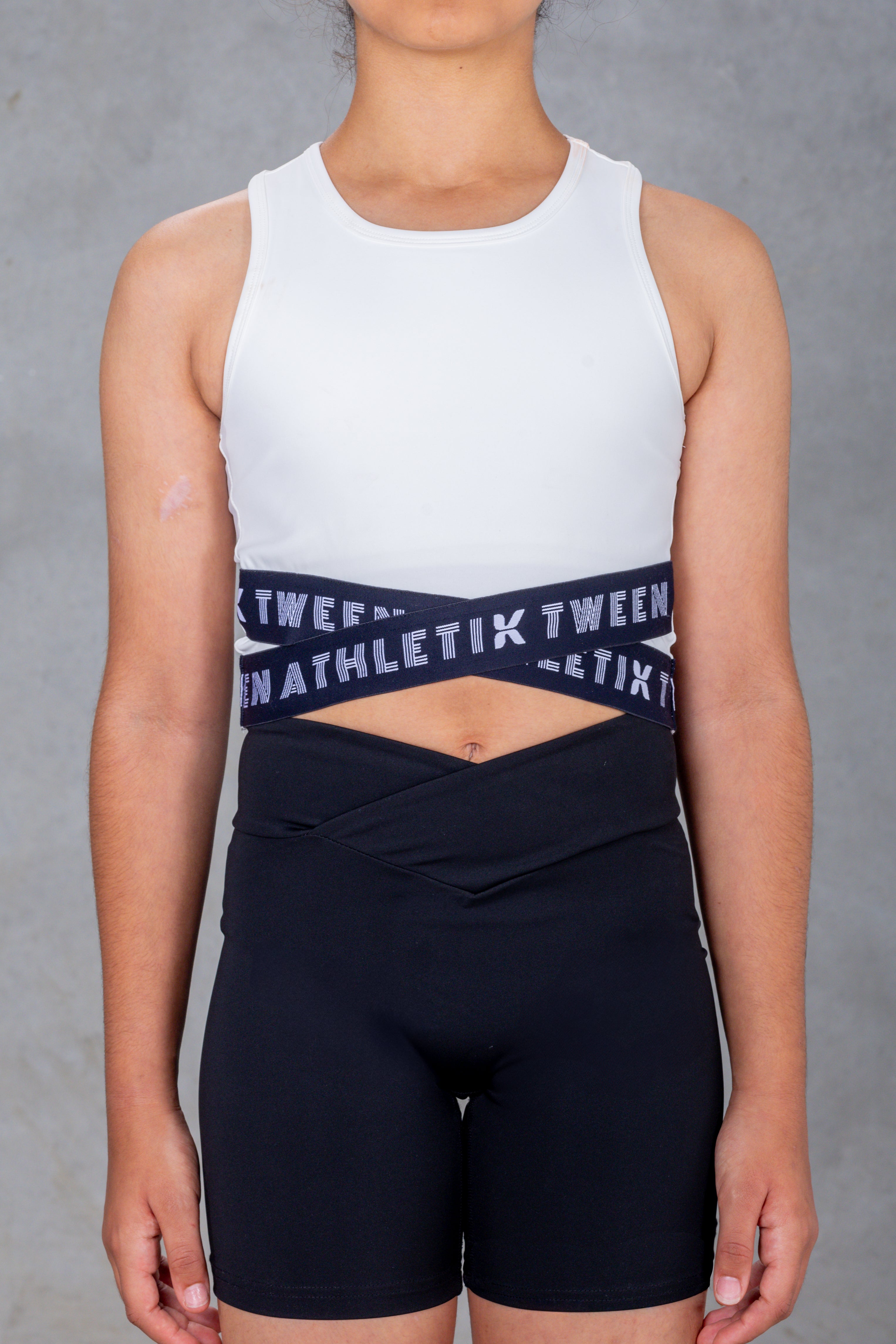 A young female model wearing a black crop top with 'ATHLETIK TWEEN' text on it.