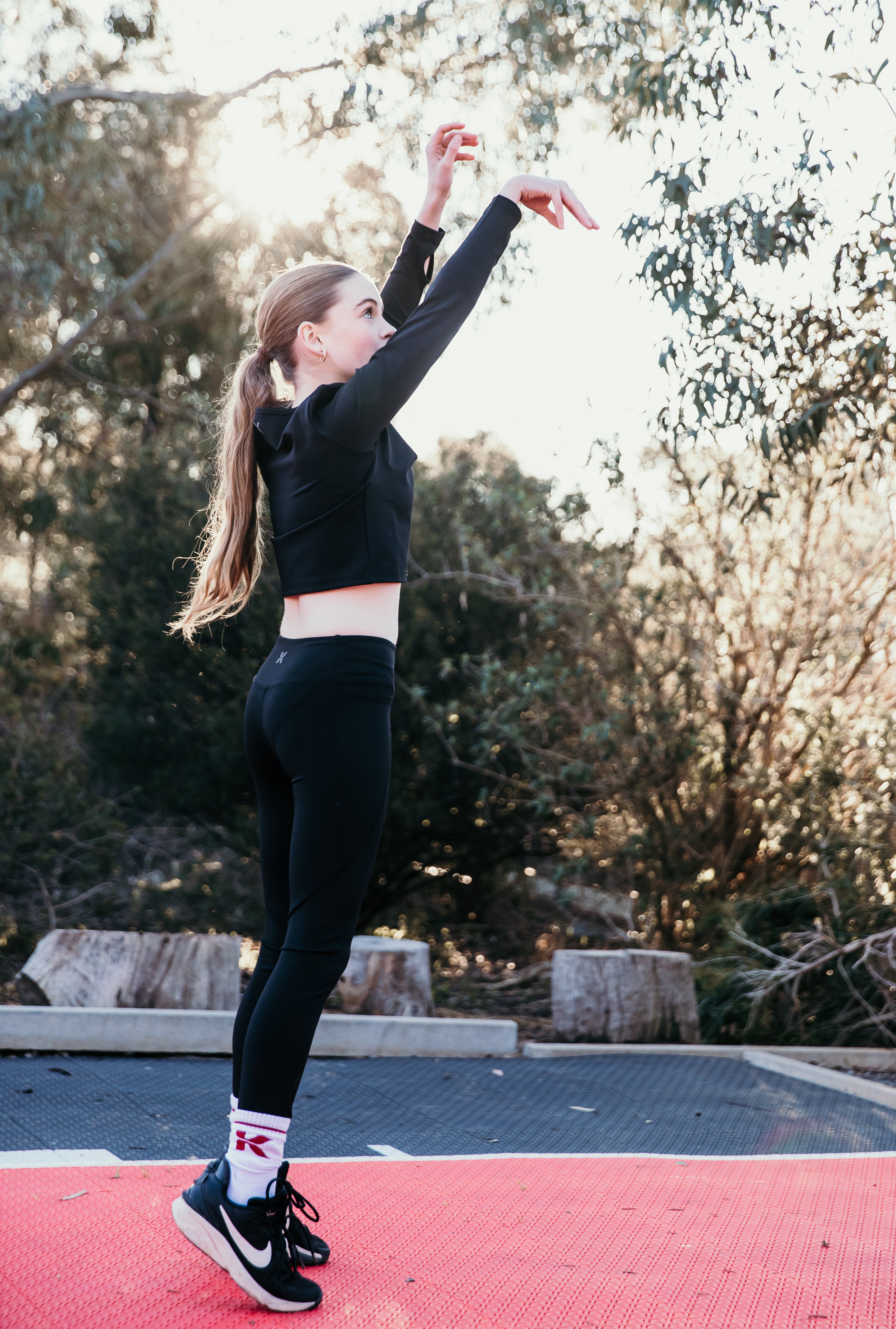 Tween stretching outdoors on a red surface with trees in the background