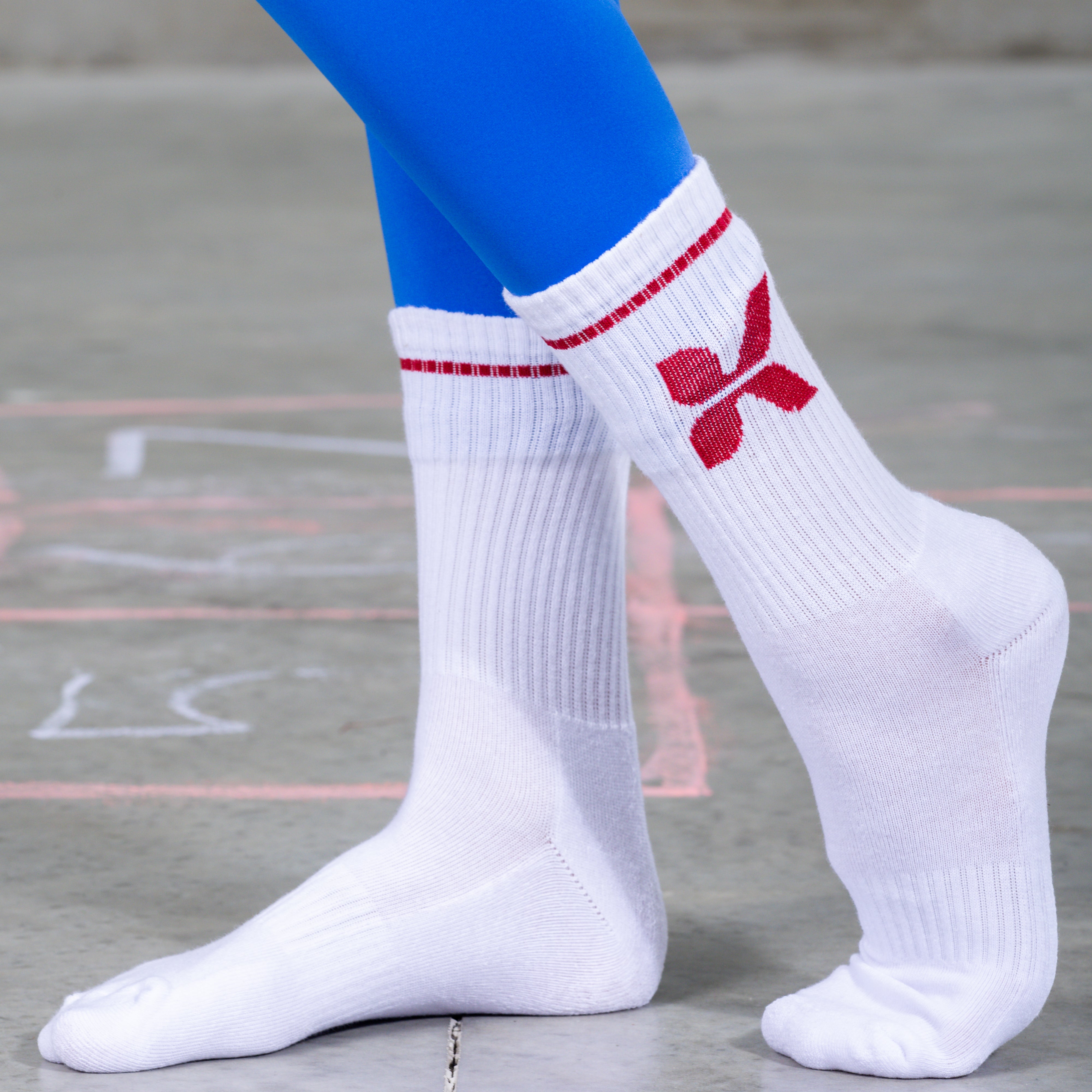 White socks with a red logo worn with blue leggings on a concrete floor.